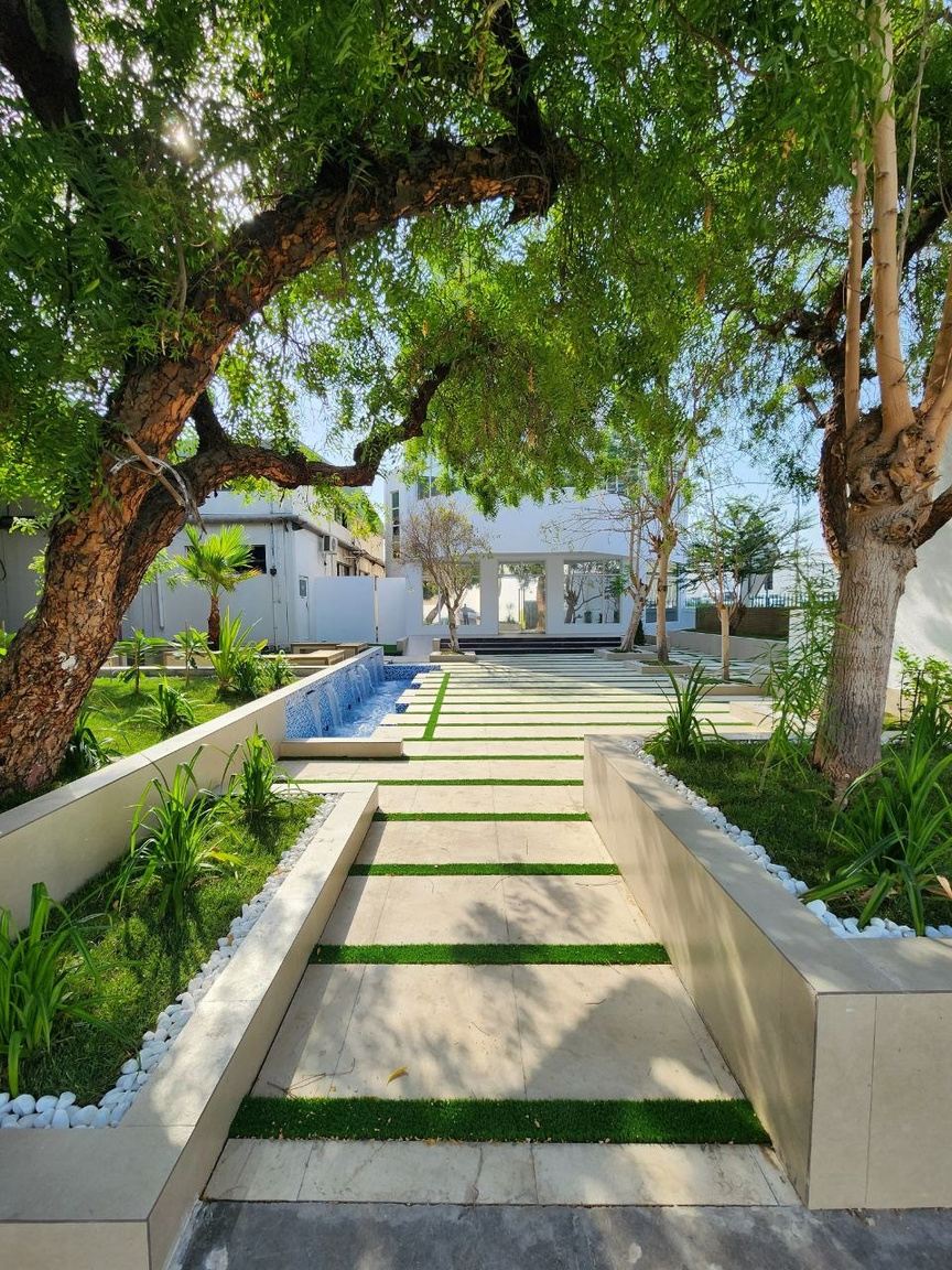 Garden walk of stepping stones in turf beside raised planters and a water channel under trees